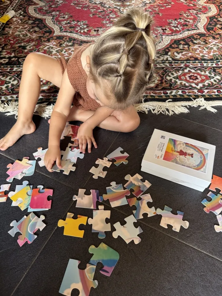 A little girl sorting the colorful pieces of her rainbow world photo puzzle next to its printed box